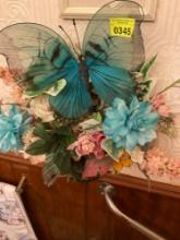 Artificial flowers and basket hanging on the bathroom Wall with the big blue butterfly in the middle